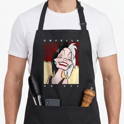 Tablier de cuisine noir avec portrait stylisé Cruella De Vil Smiling et texte CRUELLA DE VIL en lettres blanches sur fond rouge pointilliste.