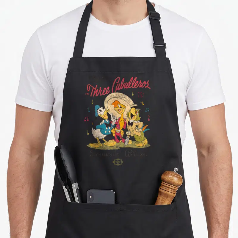 Tablier de cuisine noir avec illustration vintage des Trois Caballeros et notes de musique colorées.