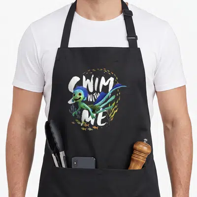 Tablier de cuisine noir avec illustration d'un monstre marin vert nageant et texte blanc Swim With Me entouré de petits poissons.