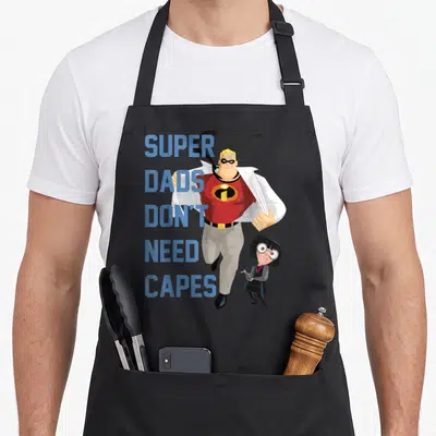 Tablier de cuisine noir avec illustration d'un papa super-héros et du texte Super Dads No Capes en bleu.