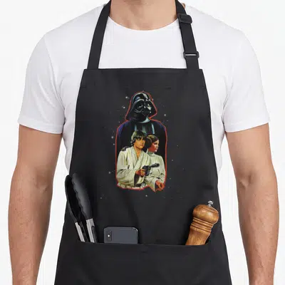 Tablier de cuisine noir avec Luke, Leia et Darth Vader en illustration vintage encadrée de rouge.