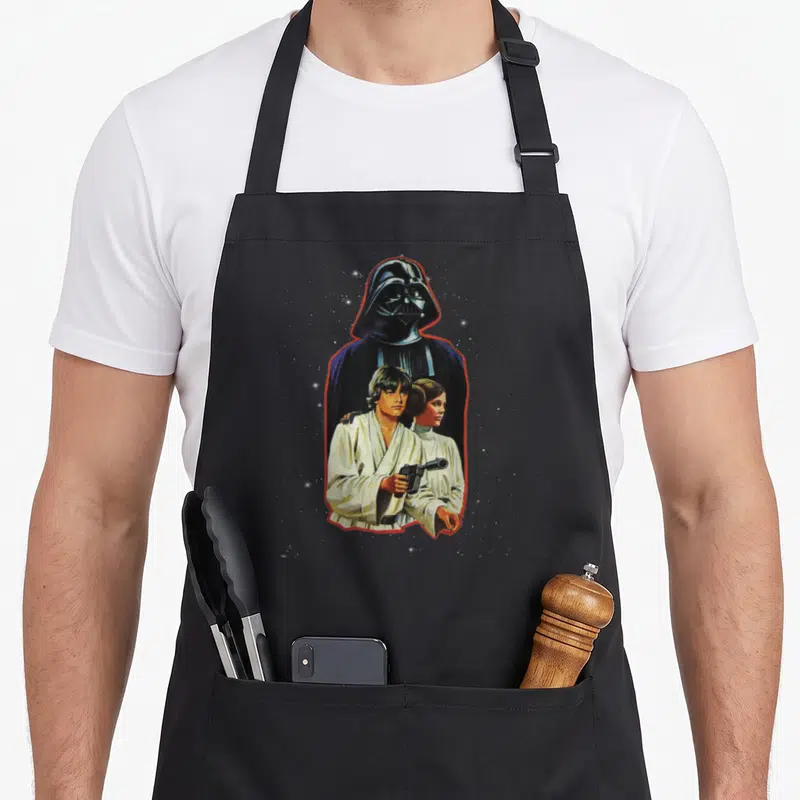 Tablier de cuisine noir avec Luke, Leia et Darth Vader en illustration vintage encadrée de rouge.
