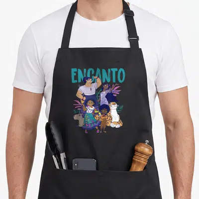 Tablier de cuisine noir avec illustration colorée des personnages d'Encanto et le titre turquoise au-dessus du groupe familial.