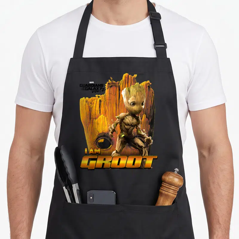 Tablier de cuisine noir avec une illustration de Groot et le texte I AM GROOT en lettres dorées sur fond bois.