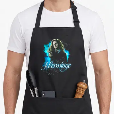 Tablier de cuisine noir avec Hermione brandissant une baguette entourée d'éclats magiques bleus et du mot Hermione en écriture cursive.