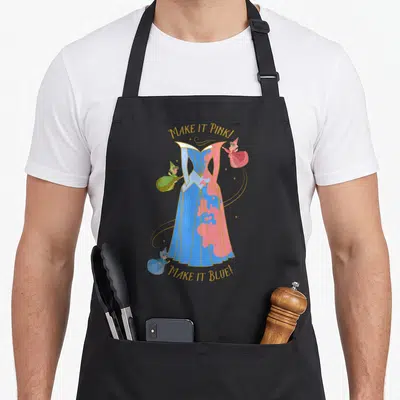 Tablier de cuisine noir avec illustration des trois fées transformant une robe bleue en rose et texte doré Make it Pink Make it Blue.