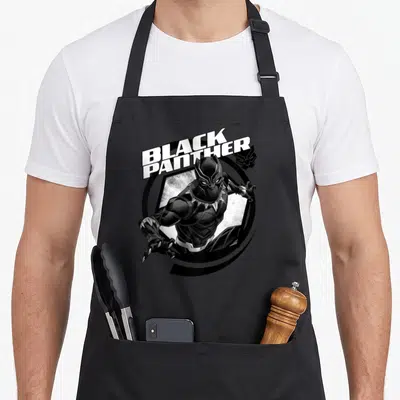 Tablier de cuisine noir avec illustration Black Panther, texte blanc et motif hexagonal circulaire.