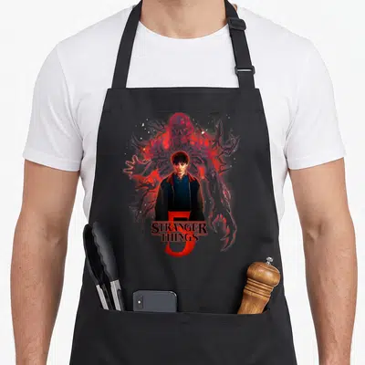 Tablier de cuisine noir avec illustration de Will et une silhouette rouge de Vecna derrière lui.