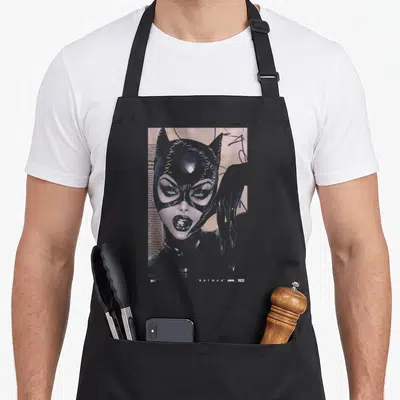 Tablier de cuisine noir avec le visage stylisé de Catwoman et la mention 85 ans en bas à droite.