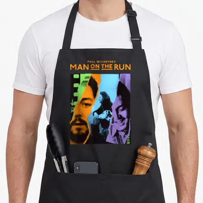 Tablier de cuisine noir avec un collage graphique coloré représentant Paul McCartney et le titre Man on the Run en orange.