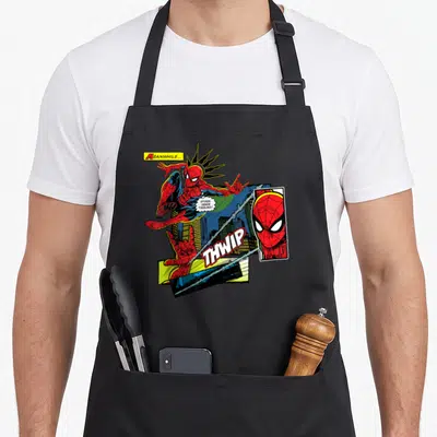 Tablier de cuisine noir avec illustration colorée de Spider-Man en action, bulles de dialogue et effets sonores style bande dessinée vintage.