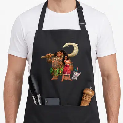 Tablier de cuisine noir illustré par Maui, Vaiana, Pua et Heihei en pleine action.