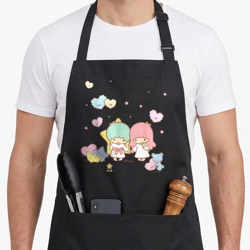 Tablier de cuisine noir avec deux personnages aux cheveux pastel tenant la main sous des étoiles colorées.