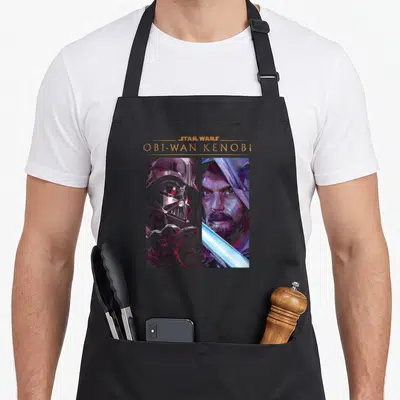 Tablier de cuisine noir avec illustration divisée montrant Vader et Obi-Wan Kenobi aux couleurs vives.