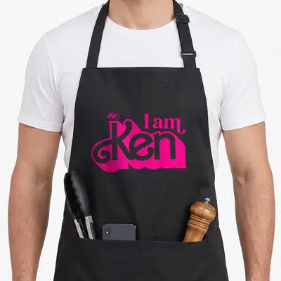 Tablier de cuisine noir avec inscription rose vif « I am Ken » en lettrage ondulé style années soixante.