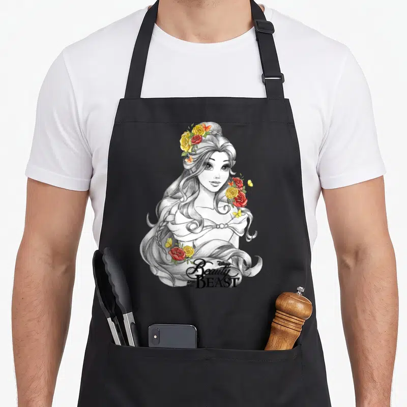 Tablier de cuisine noir avec portrait de Belle esquissé, roses colorées et titre « Beauty and the Beast » en bas.