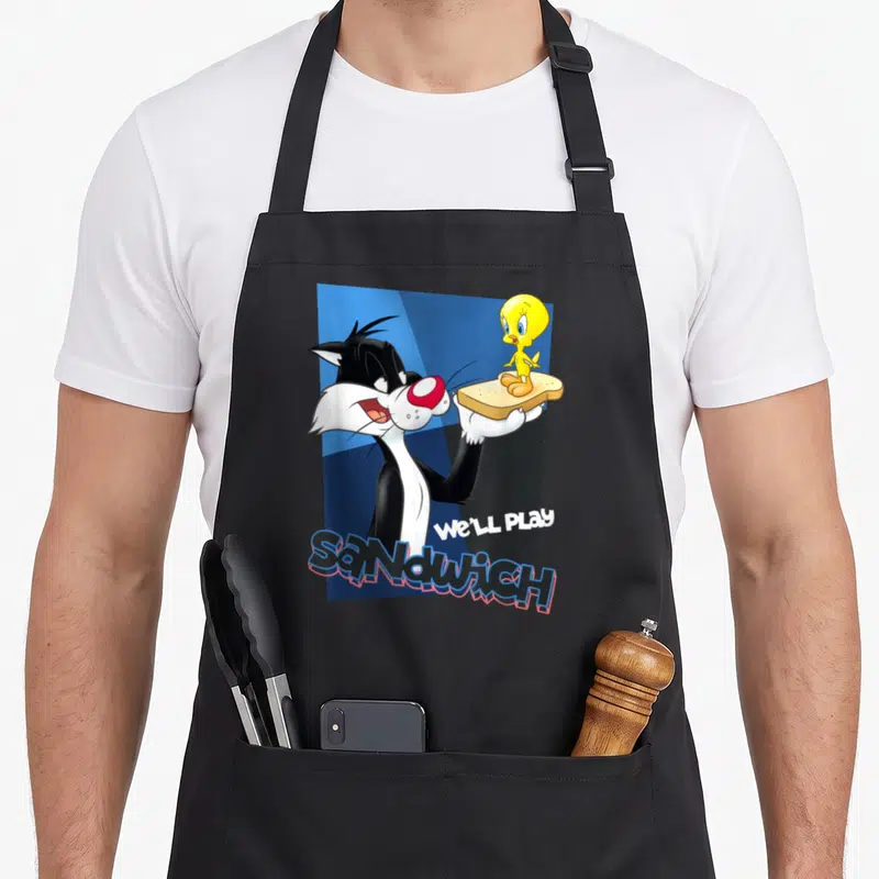Tablier de cuisine noir avec Sylvester tenant Tweety sur du pain et le texte We'll play sandwich.