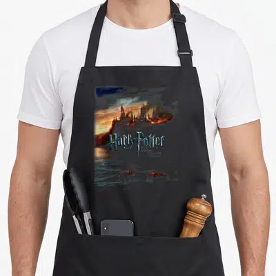 Tablier de cuisine noir avec illustration du château d'Harry Potter en feu et le titre du film imprimé au centre.