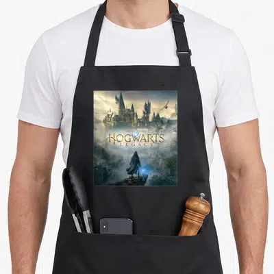 Tablier de cuisine noir avec une illustration du château de Poudlard et un personnage tenant une baguette magique luminescente.
