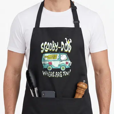 Tablier de cuisine noir avec illustration colorée de la Mystery Machine et du texte Scooby-Doo Where Are You en lettres stylisées.
