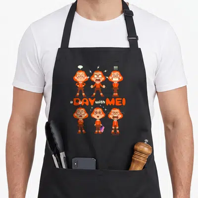 Tablier de cuisine noir avec six illustrations de Mei aux expressions variées et le texte a Day with Mei en orange.
