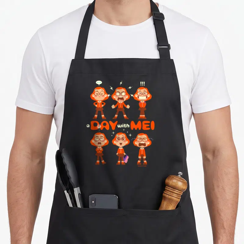 Tablier de cuisine noir avec six illustrations de Mei aux expressions variées et le texte a Day with Mei en orange.