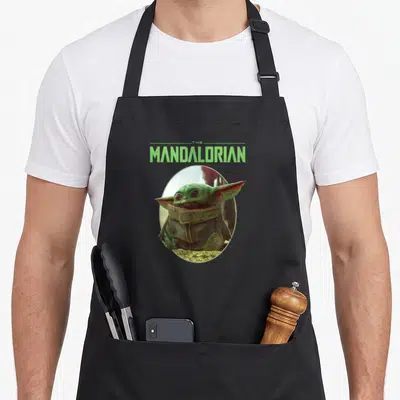 Tablier de cuisine noir avec un portrait ovale de Grogu et le logo The Mandalorian en vert lime au-dessus.