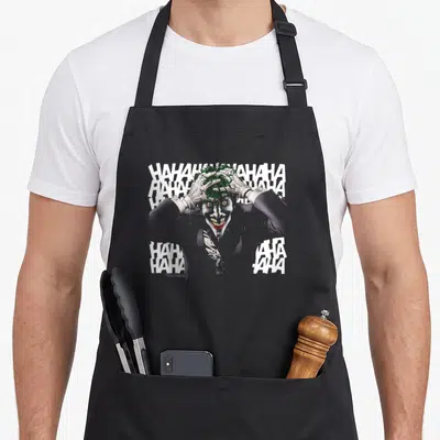 Tablier de cuisine noir avec illustration du Joker et texte HAHAHA blanc en arrière-plan.