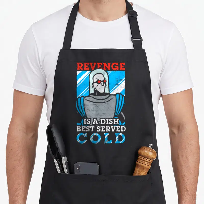Tablier de cuisine noir avec illustration vintage de Mr. Freeze et texte Revenge is a dish best served cold en bleu et rouge.