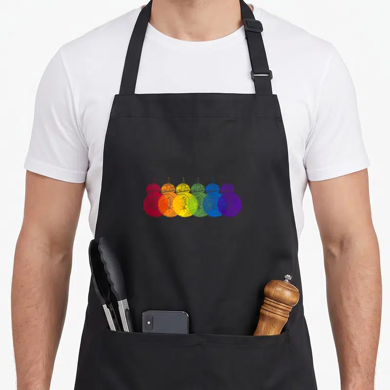 Tablier de cuisine noir avec une illustration de six robots BB-8 superposés aux couleurs vives de l'arc-en-ciel sur fond gris uni.