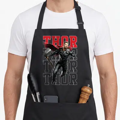Tablier de cuisine noir avec illustration Thor marteau et texte rouge en arrière-plan typographique.