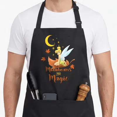 Tablier de cuisine noir avec Tinkerbell sur une feuille, lune jaune et texte Moonbeams and Magic orange.