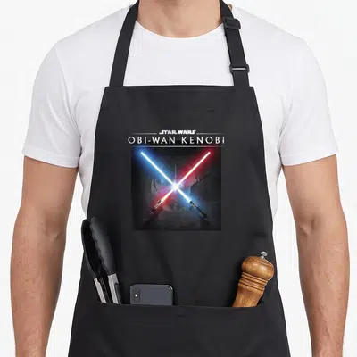 Tablier de cuisine noir avec illustration de deux sabres laser bleu et rouge croisés sous le nom Obi-Wan Kenobi.