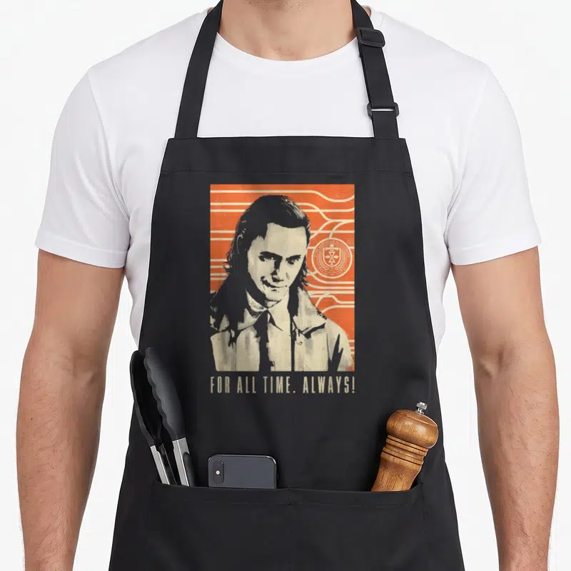 Tablier de cuisine noir avec portrait rétro de Loki, lignes ondulées orange et logo circulaire du TVA sur fond uni.