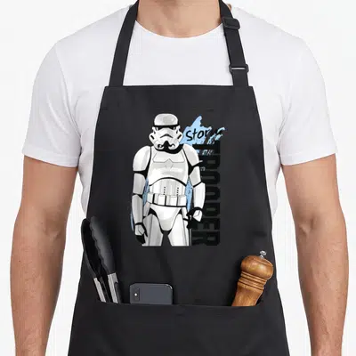 Tablier de cuisine noir avec illustration Storm Trooper et texte vertical Storm TROOPER sur fond bleu clair.