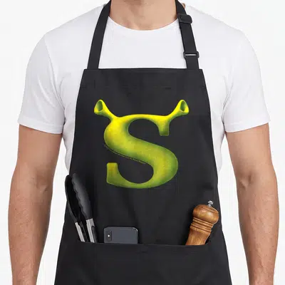 Tablier de cuisine noir avec une grande lettre S verte texturée aux extrémités ressemblant à des oreilles d'elfe