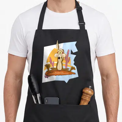 Tablier de cuisine noir avec illustration du Coyote assis dans un décor de désert aux couleurs vives.