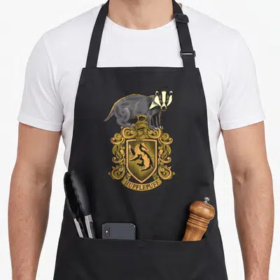 Tablier de cuisine noir avec illustration d'un badger sur un écu doré et l'inscription Hufflepuff