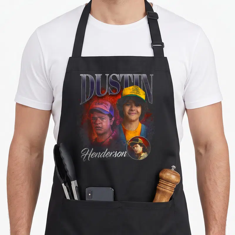 Tablier de cuisine noir avec illustration de Dustin Henderson et son casque jaune typique.
