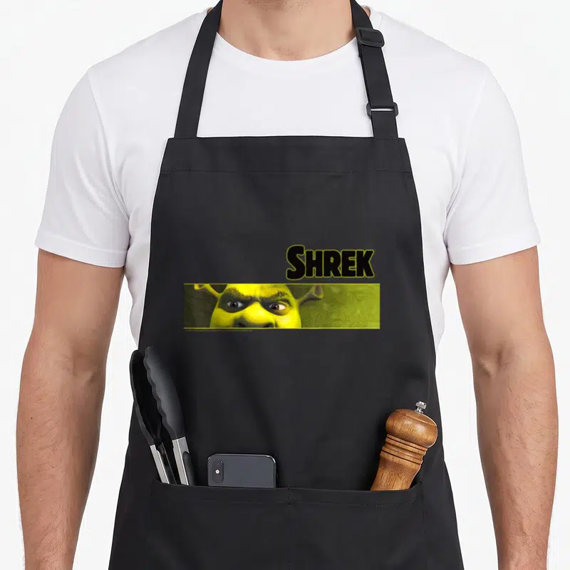 Tablier de cuisine noir avec le logo Shrek et un gros plan sur les yeux verts et menaçants de l'ogre.