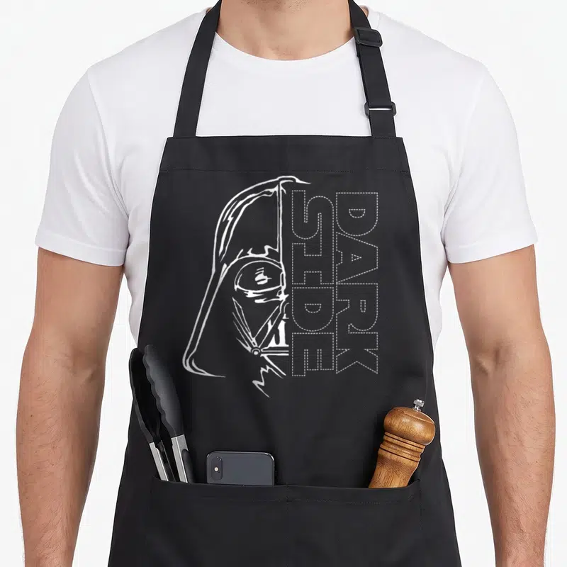 Tablier de cuisine noir avec illustration blanche de Dark Vador et texte Dark Side Two Face Stitch en pointillés.