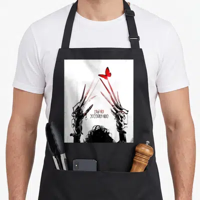 Tablier de cuisine noir avec des ciseaux métalliques formant un cœur sous un papillon rouge vif.