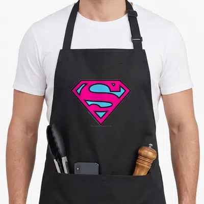 Tablier de cuisine noir avec le logo Superman rose et bleu au centre.