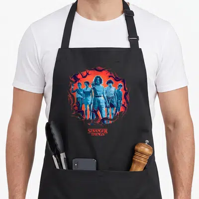 Tablier de cuisine noir avec illustration des personnages Eleven, Lucas, Mike et Dustin sur fond rouge et bleu.