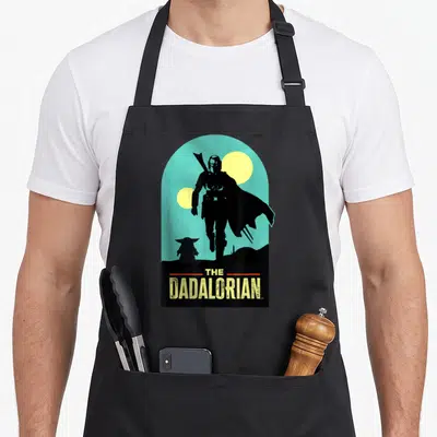 Tablier de cuisine noir avec silhouette Mandalorian Grogu et texte The Dadalorian sur fond turquoise.