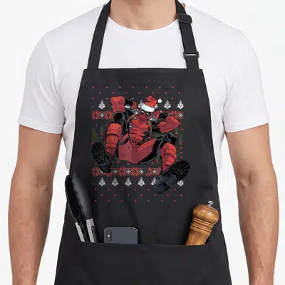 Tablier de cuisine noir avec Deadpool en saut portant un bonnet de Père Noël sur fond de motifs de Noël pixelisés.