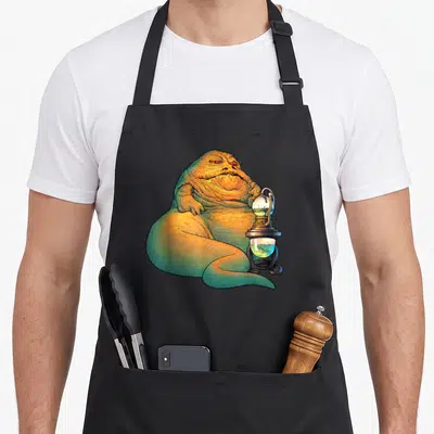 Tablier de cuisine noir avec Jabba le Hutt assis près d'une lanterne à liquide vert brillant.