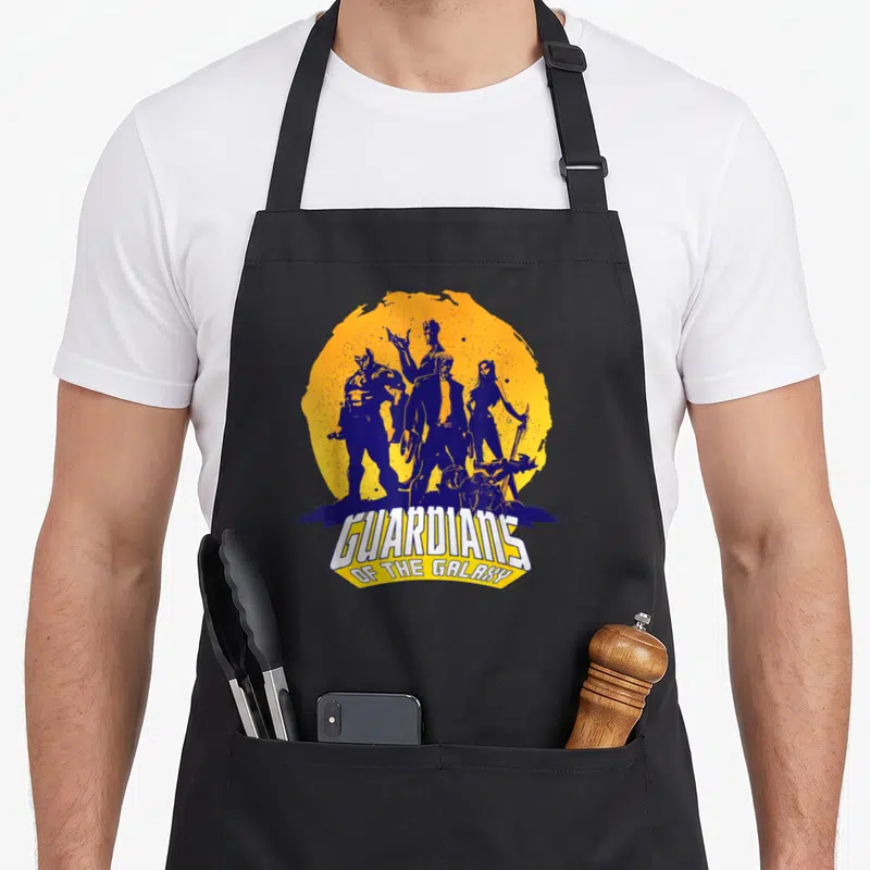 Tablier de cuisine noir avec illustration vintage des Gardiens de la Galaxie et leur logo en blanc et jaune sur fond circulaire orange.