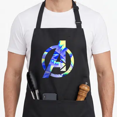 Tablier de cuisine noir avec logo Avengers rempli de motifs de feuilles tropicales bleues et jaunes.