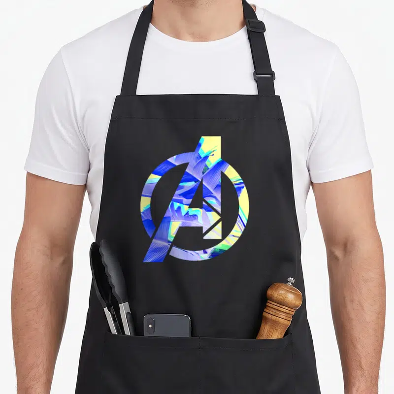 Tablier de cuisine noir avec logo Avengers rempli de motifs de feuilles tropicales bleues et jaunes.
